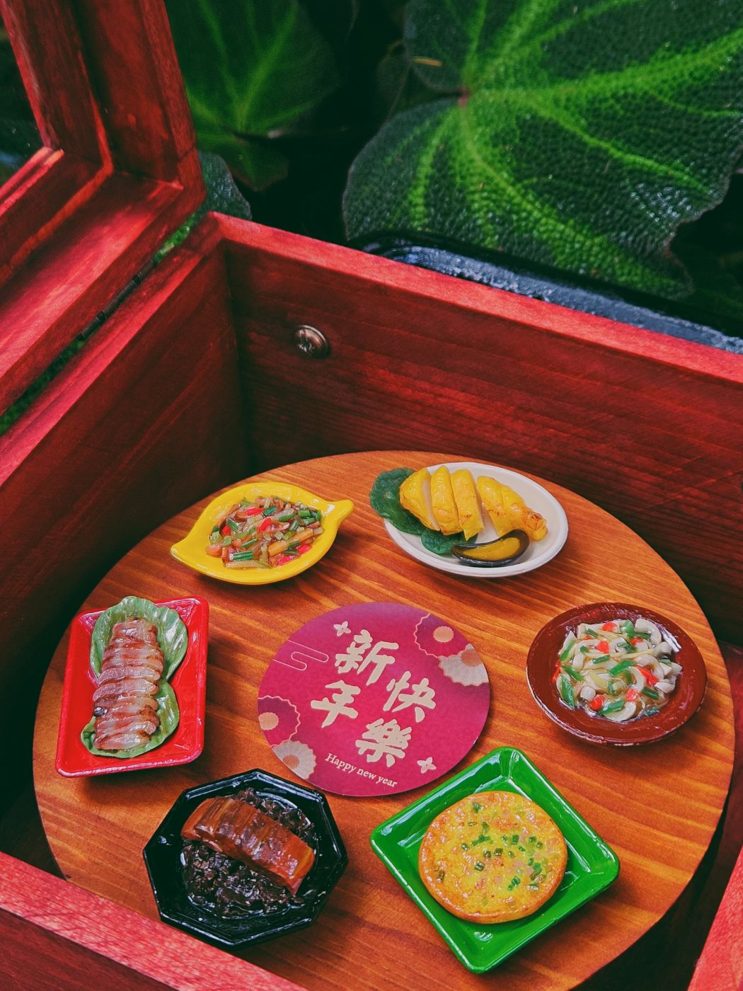 打開的木盒，六道袖珍年菜圍繞新年快樂卡